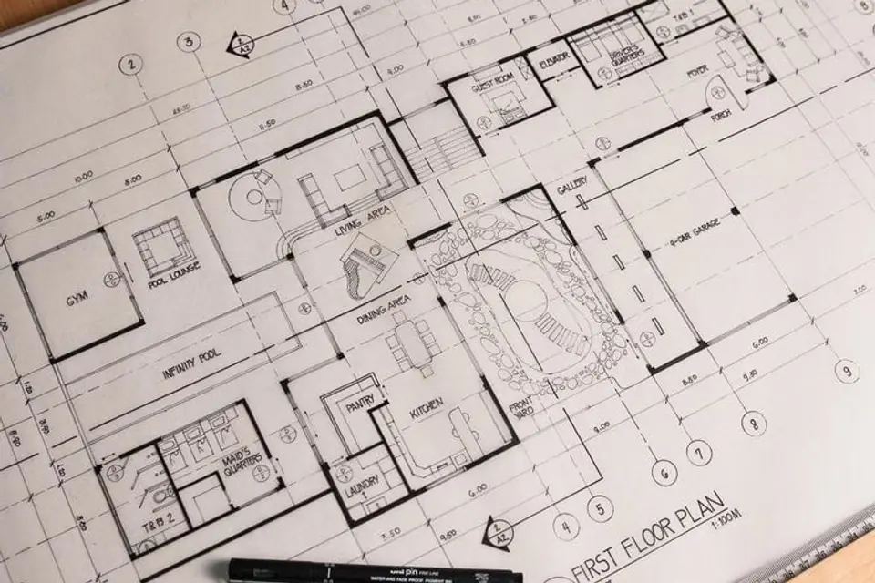 A residential floor plan on the drawing board with drafting pens and a scale rule