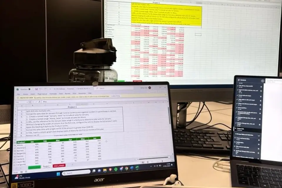 A project schedule open across a desktop monitor and laptop at a work desk